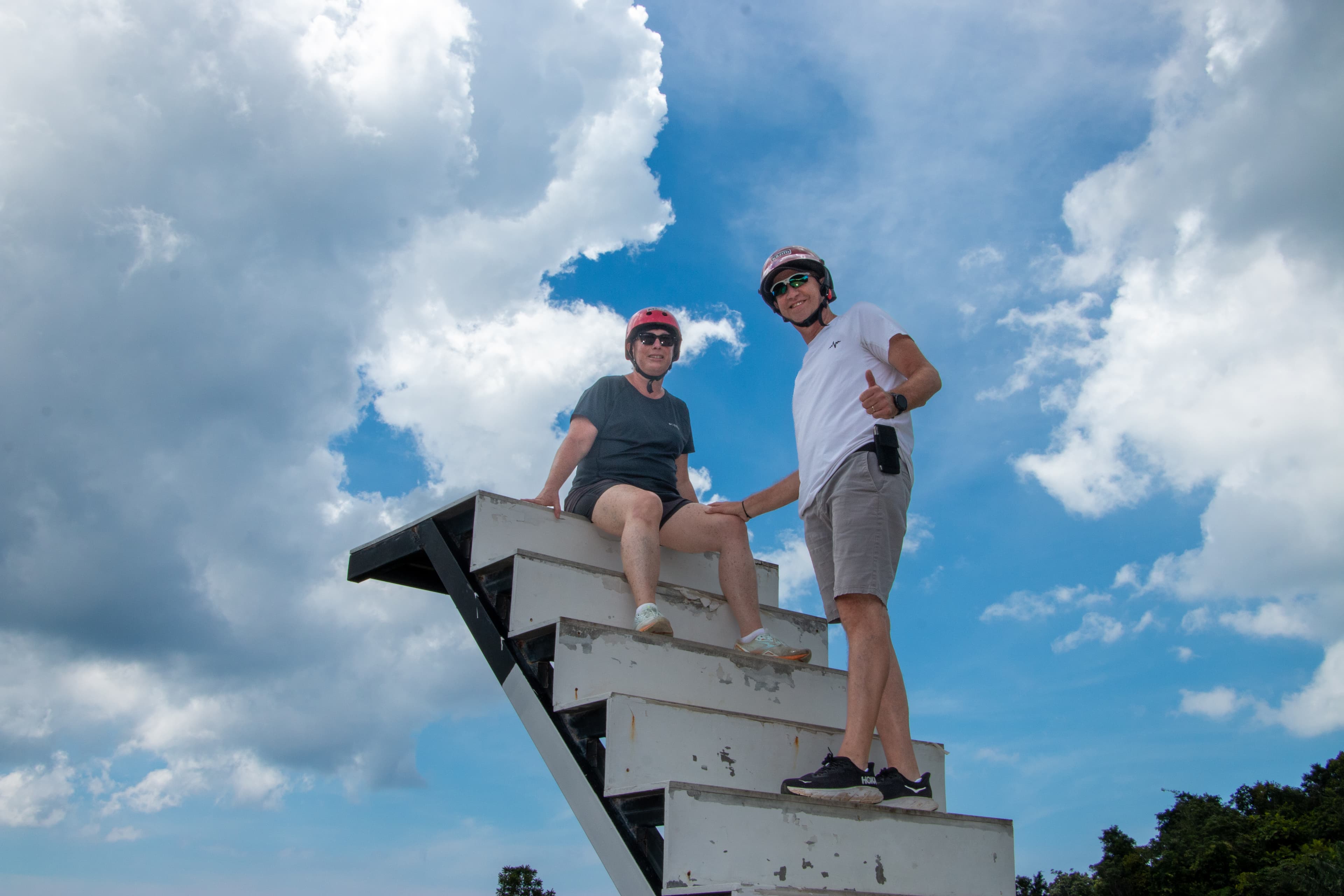 Two guests on a high zipline stairway with dramatic sky